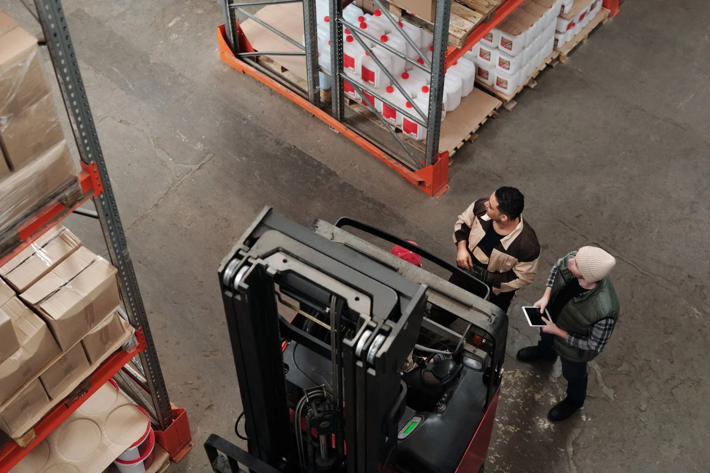 Two warehouse colleagues checking information together beside a forklift